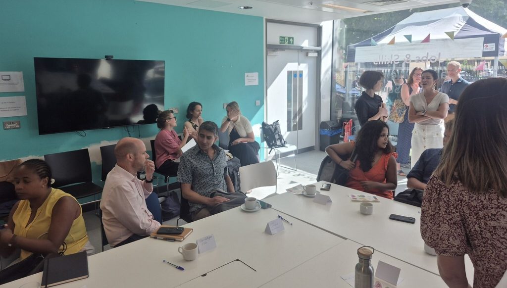 Image shows a workshop room with a large glass window and around 20 people gathering insight, speaking to one another.
